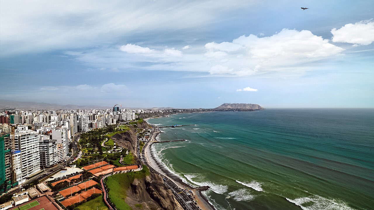 Aerial view of the Miraflores clifftop district of Lima above a long grey-green stretch of Pacific coastline