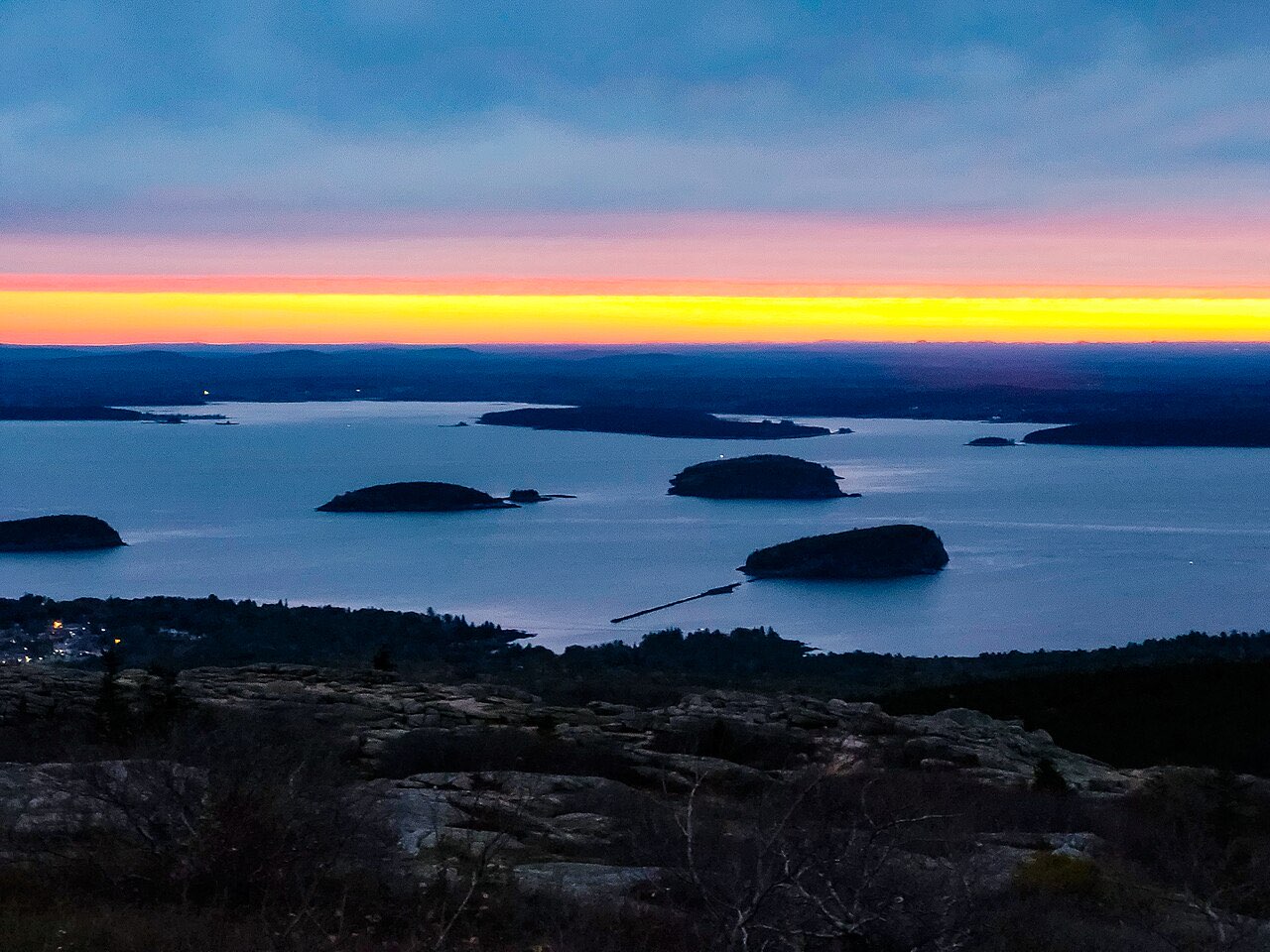 Dawn sky over islands and water seen from the bare granite summit of Cadillac Mountain in Acadia National Park