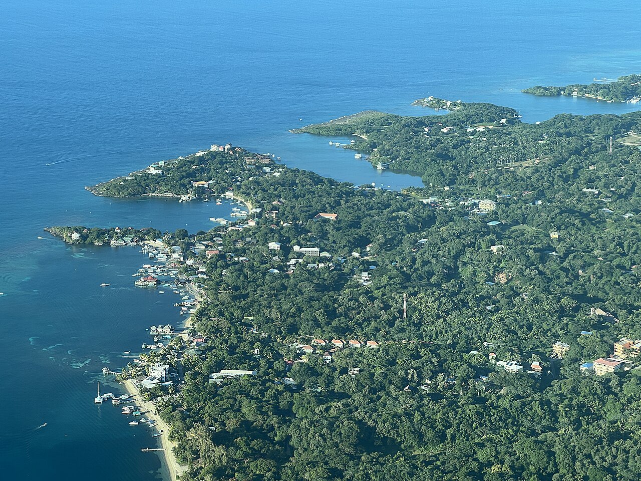 Aerial view of a forested headland with houses and small docks along a narrow bay at West End, Roatan